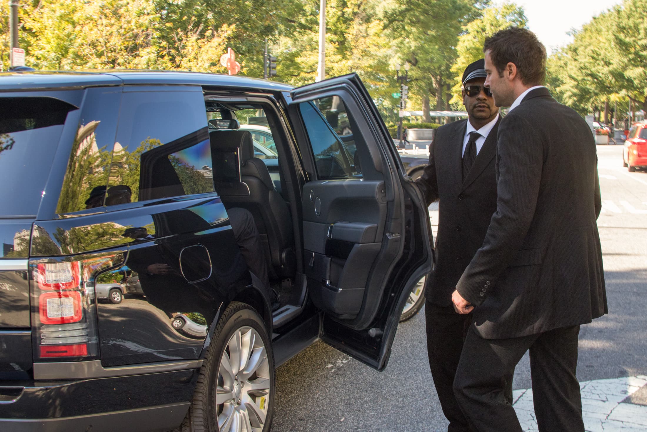 Executive protection detail escorting a client to an armored Alpine Armoring rental vehicle